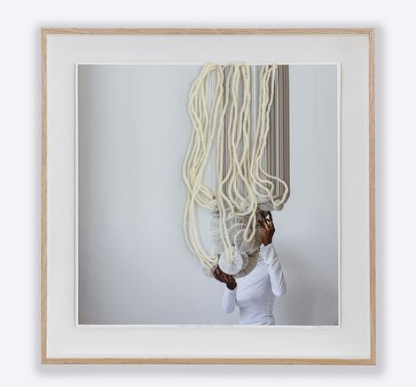 Person in white top holding two round, pleated objects under hanging long white ropes.