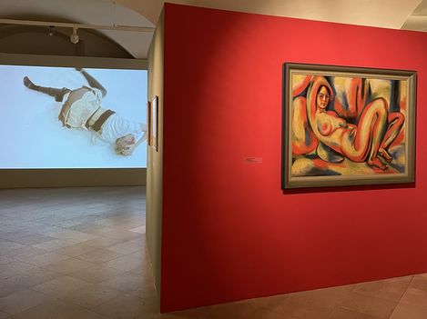 Exhibition view with a projection of a reclining figure on the wall and a painting of a nude figure on a red wall.