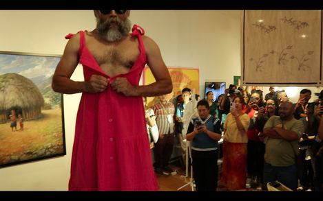 Mann mit rotem ärmellosem Kleid, der vor einer Gruppe von Menschen in einem Raum mit Kunstwerken steht
