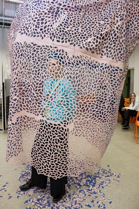 Person standing inside a large perforated paper structure with organic patterns.