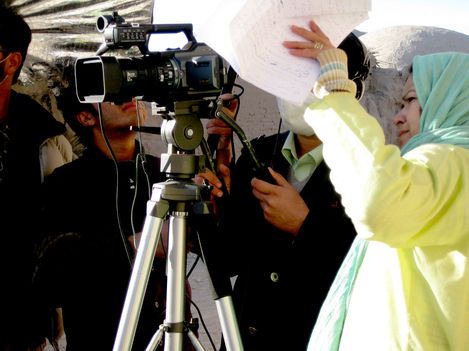 People operate a video camera on a tripod, one person holds up papers.