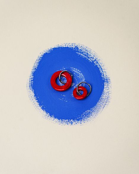 Two round earrings with red plastic rings on a blue paint spot on a light background