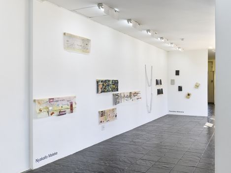 White exhibition room with several abstract artworks on the wall and dark stone floor.