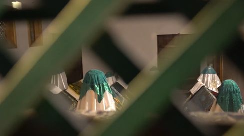View through a lattice showing three people wearing headscarves kneeling before an altar or religious setting.