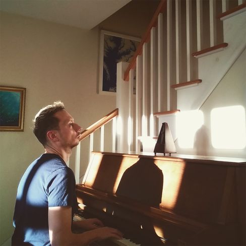 Mann sitzt an einem Klavier in einem Raum mit Treppe und Bildern an der Wand.