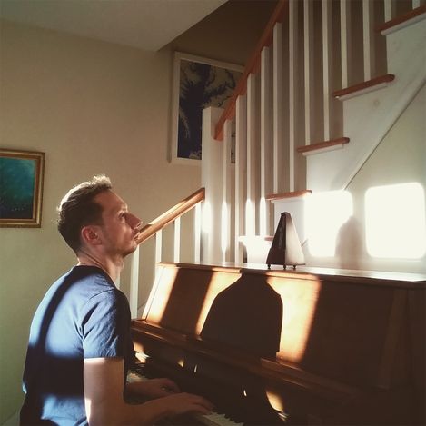 Mann sitzt an einem Klavier in einem Raum mit Treppe und Bildern an der Wand.