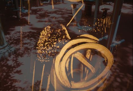 Gold brushstrokes and speckles on a dark reflective surface with columns in the background.