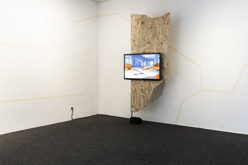 Monitor displaying a digital landscape animation, mounted on a wooden panel in a white corner space.