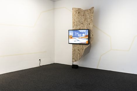 Monitor displaying a digital landscape animation, mounted on a wooden panel in a white corner space.