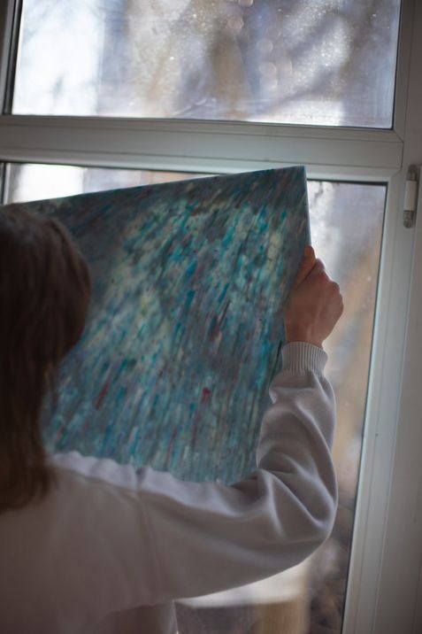 Person holding a rectangular transparent object with blue and green patterns up to a window