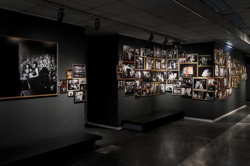 Dimly lit exhibition room with numerous black-and-white photographs of various people and scenes on the walls.