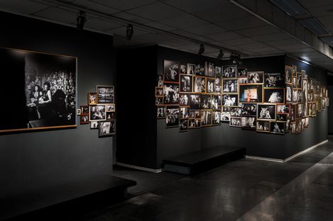 Dimly lit exhibition room with numerous black-and-white photographs of various people and scenes on the walls.