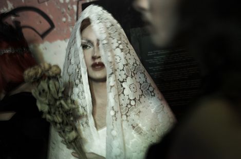 Person with white lace fabric over their head holding a dried bouquet in a dimly lit setting.