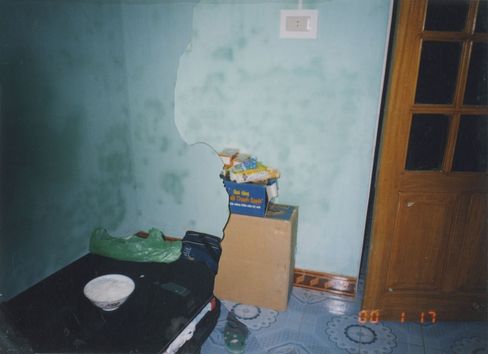 Kleiner Raum mit blassblauer Wand, Kartons und Taschen auf dem Boden neben einer Holztür mit Glasfenstern.