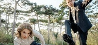 Zwei Personen in formeller Kleidung posieren auf einem Waldweg, eine hockt, die andere hebt ein Bein hoch.