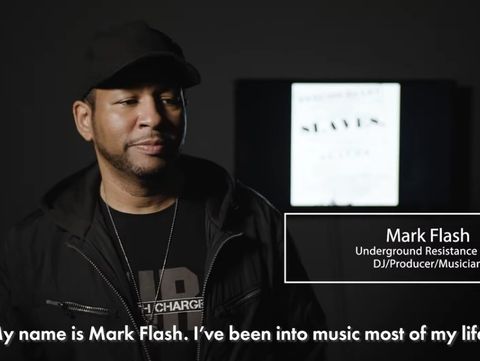 Man in a dark jacket and cap speaks confidently against a blurred backdrop. Text overlay identifies him as Mark Flash, an Underground Resistance DJ/Producer.