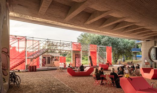 Rote Enzi-Sitzmöbel unter einer Brücke, Menschen sitzen und essen an roten Tischen, im Hintergrund ein temporärer Pavillon mit der Aufschrift „Southbank“.