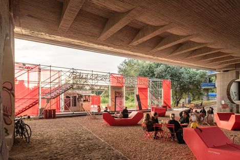 Rote Enzi-Sitzmöbel unter einer Brücke, Menschen sitzen und essen an roten Tischen, im Hintergrund ein temporärer Pavillon mit der Aufschrift „Southbank“.