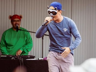 The two musicians, Brudi and Bär, are standing on a small stage. Bär is sitting at the mixing desk, whilst Brudi is standing in the foreground holding a microphone.