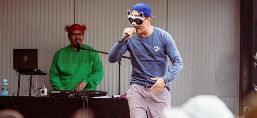 The two musicians, Brudi and Bär, are standing on a small stage. Bär is sitting at the mixing desk, whilst Brudi is standing in the foreground holding a microphone.
