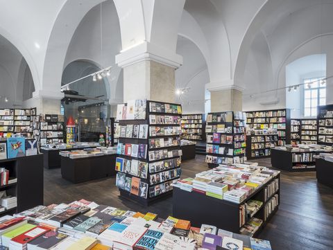 Spacious bookstore with high arched ceilings, filled with neatly organized shelves and tables of books. Bright lighting and a serene atmosphere.