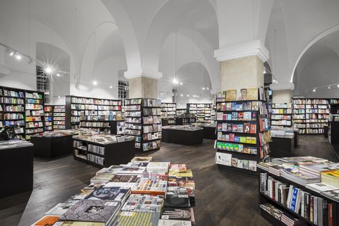 Spacious bookstore with high arched ceilings, filled with neatly organized shelves and tables of books. Bright lighting and a serene atmosphere.