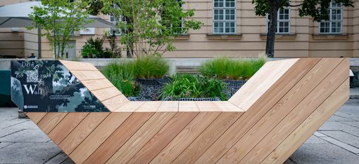 Wooden Enzi seating element at MuseumsQuartier Vienna, set among planted beds in front of a historic building façade.