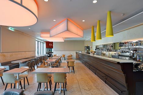 Interior view of Café Leopold showing the bar area, wooden tables and chairs, modern lighting and a bright, open atmosphere.