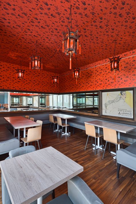 Seating area in Café Leopold featuring red patterned walls, Asian-inspired lanterns, and a view of the bar and lounge area.