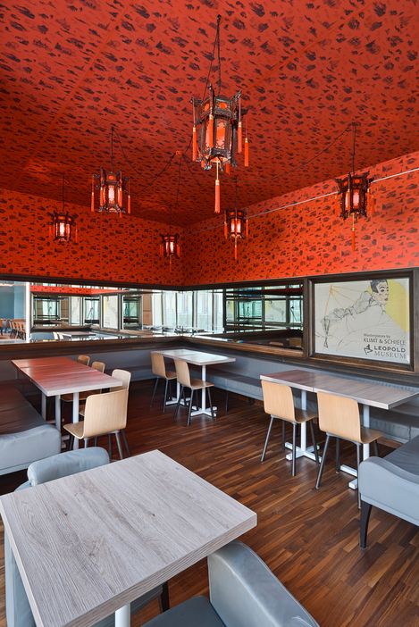 Seating area in Café Leopold featuring red patterned walls, Asian-inspired lanterns, and a view of the bar and lounge area.