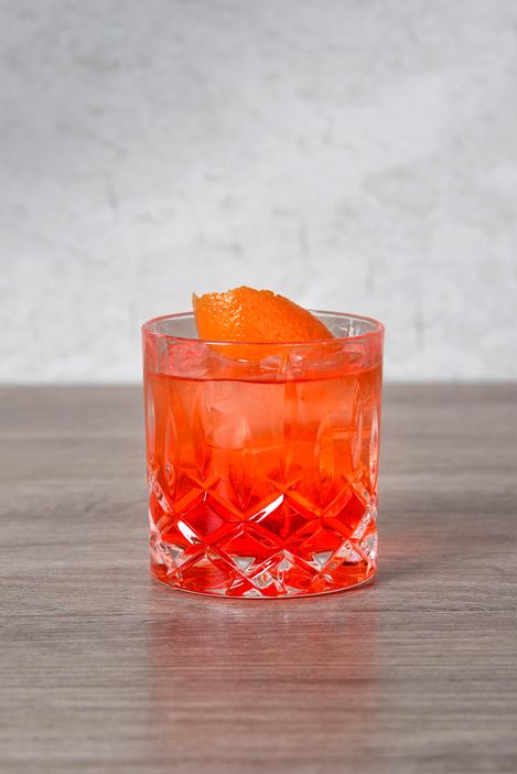 Negroni cocktail in a cut glass with ice cubes and orange peel on a wooden table