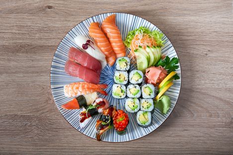 Sushi platter with nigiri and maki featuring salmon, tuna, shrimp and avocado on a round plate