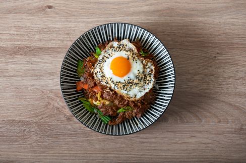 Bowl with spicy marinated meat, rice, fried egg and vegetables, top view