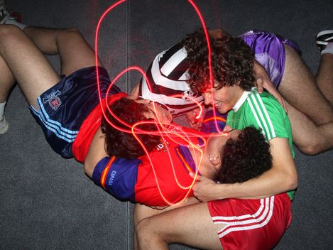 Drei junge Männer in Sportkleidung liegen auf dem Boden und lachen.