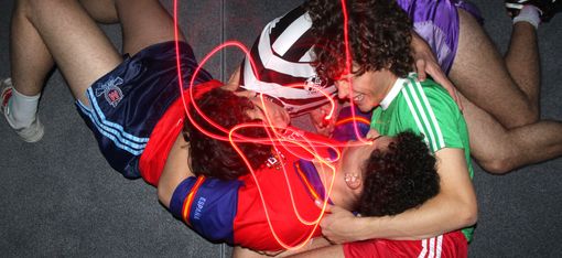 Drei junge Männer in Sportkleidung liegen auf dem Boden und lachen.