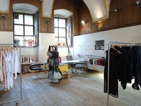 Interior of a store with wooden floor, tall windows, clothing racks, and a table with chairs
