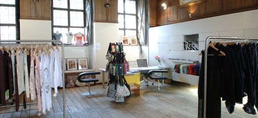 Interior of a store with wooden floor, tall windows, clothing racks, and a table with chairs