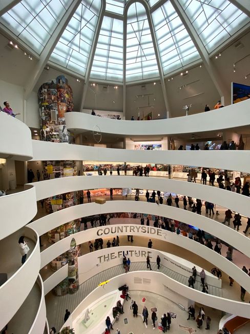 Interior view of the Guggenheim Museum with a spiraling gallery and visitors on multiple levels under a large glass dome.