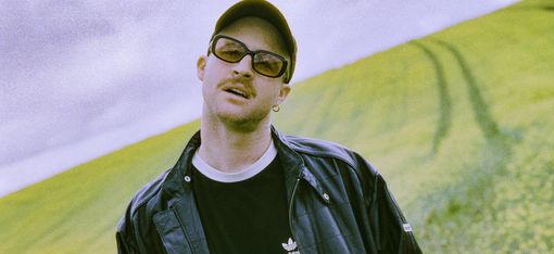Young man wearing a black Adidas jacket and black T-shirt standing in front of a hilly landscape