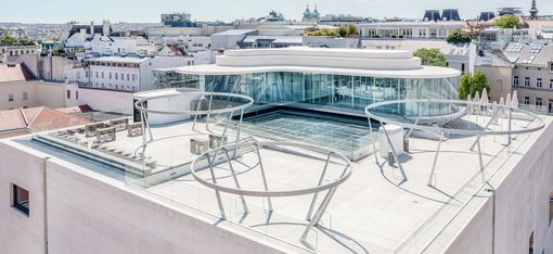 Modern rooftop terrace with a glass façade and delicate metal structures overlooking the rooftops of Vienna.
