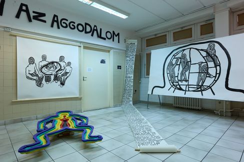 Exhibition with black-and-white line drawings of figures and a long scroll of text in a bright room with tiled floor