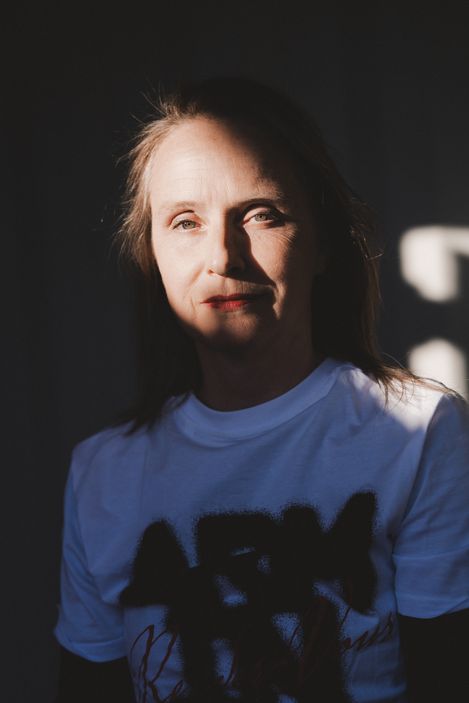 Frau mit langem Haar und weißem T-Shirt steht vor dunklem Hintergrund mit Schatten auf dem Gesicht