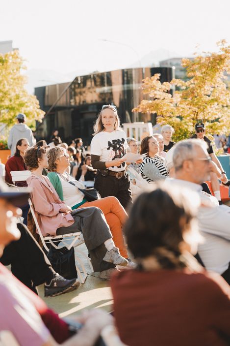 Menschen sitzen und stehen im Freien bei sonnigem Wetter vor einem modernen Gebäude mit Glasfassade