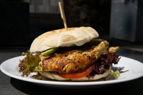 Close-up of a sandwich with grilled chicken, lettuce, tomato, and avocado on a white plate.