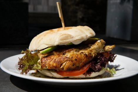 Close-up of a sandwich with grilled chicken, lettuce, tomato, and avocado on a white plate.