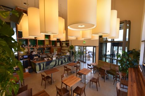 Interior of a café with wooden tables, chairs, a bar with shelves, and several round ceiling lights