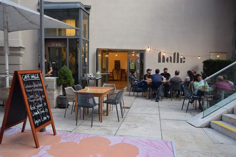 Outdoor seating area of a café with several tables and chairs and a group of people sitting at one table with a handwritten menu board