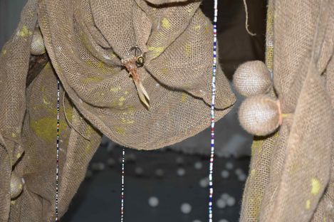 Close-up of coarse woven fabric with beaded strings and two spherical objects made of the same material.