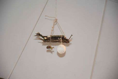 A hanging mobile made of a branch, a small figure, and a ball, all suspended by strings.