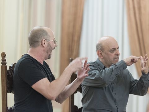 The artists are sitting side by side on chairs and gesturing.